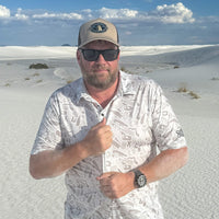 Man in a camo patterned shirt and showing the shirts stretch in a desert landscape